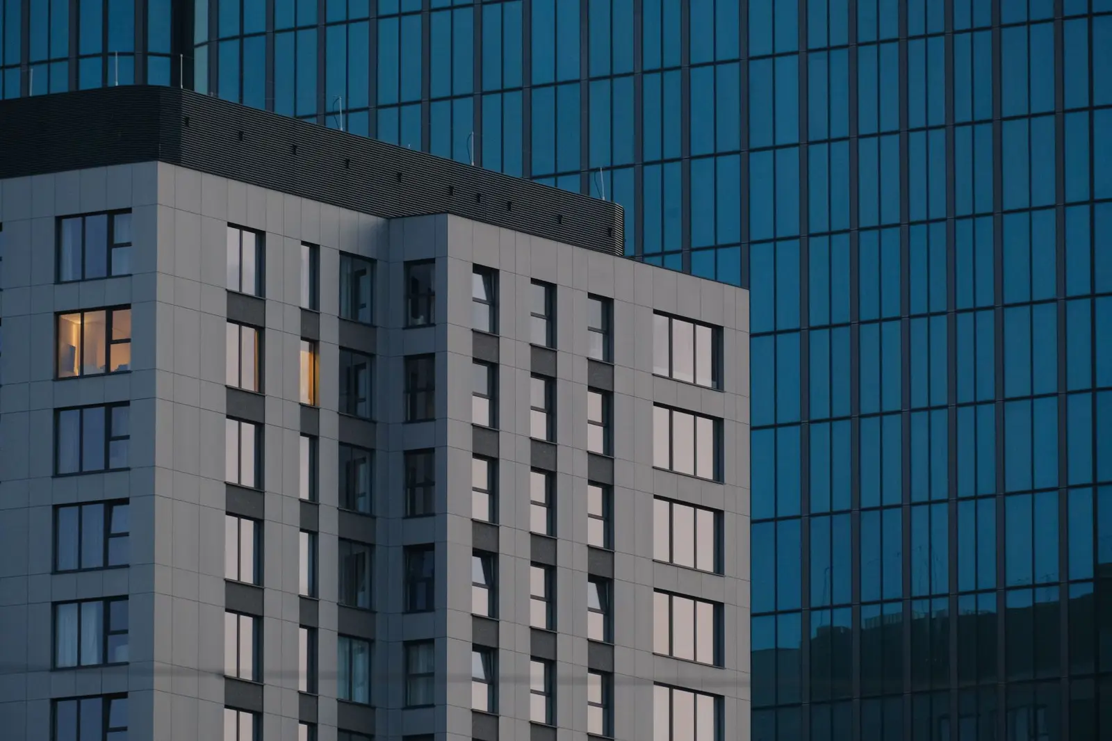 Modern glass office tower at twilight with illuminated windows.