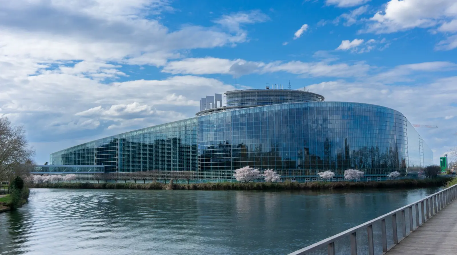 Modern government building with a blue glass facade reflected in a river.